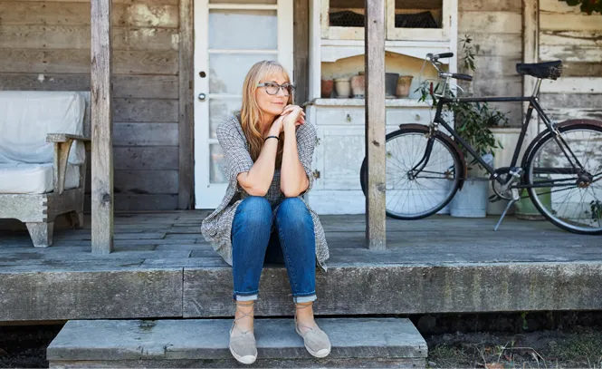 A middle aged woman sitting on a rustic porch.
