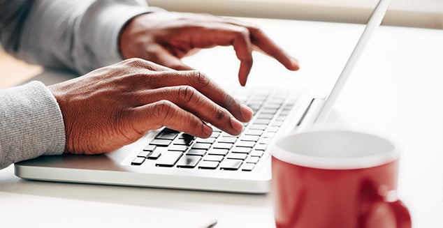 A man's hands typing on a laptop keyboard to enter information into myOrangeMoney