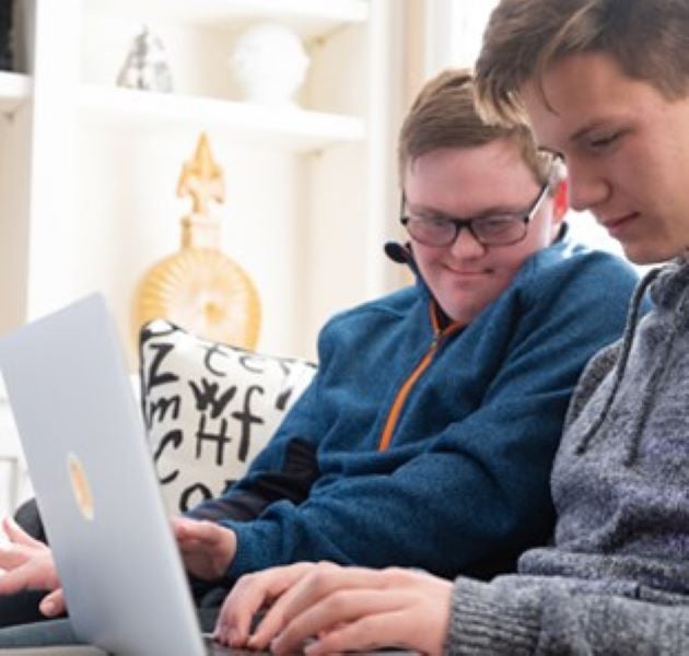 Two boys, one with Down Syndrome looking at laptop while sitting on the couch