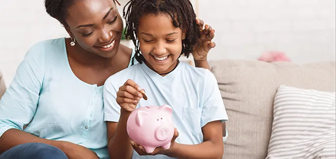 Money Saving Concept. Happy black mom and daughter inserting coins in pink piggy bank, empty space