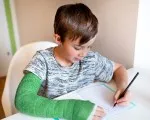 Young boy drawing on a piece of paper, with a broken arm.