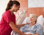 An older woman in a hospital bed talking with her nurse.