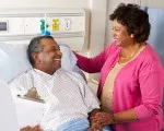 An older man in a hospital bed looking at his wife.