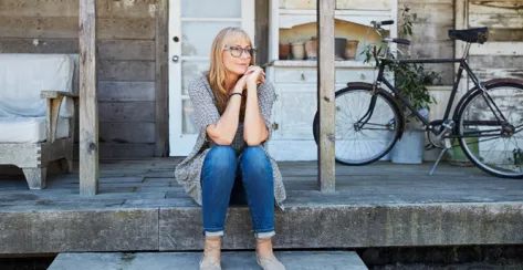 A middle aged woman sitting on a rustic porch.