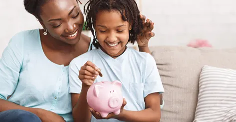 Money Saving Concept. Happy black mom and daughter inserting coins in pink piggy bank, empty space