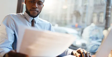 Black millennial male employee analyzes documents in an urban cafe.