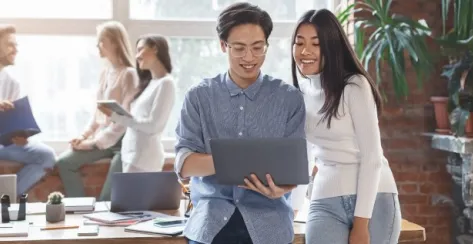 Excited Asian man sharing business ideas on a laptop with a young mixed race woman coworker in an office setting