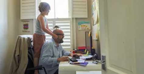 Dad working in home office   with a toy dinosaur on his head being distracted by his young son