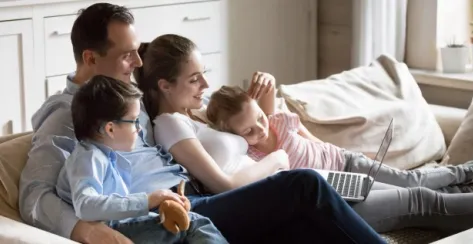 Parents on a sofa cuddling with their two young children while watching a video on a laptop