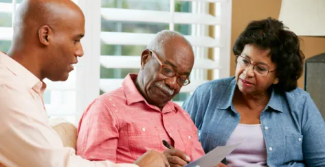 Older black couple signing paper forms under the watch of a younger man.