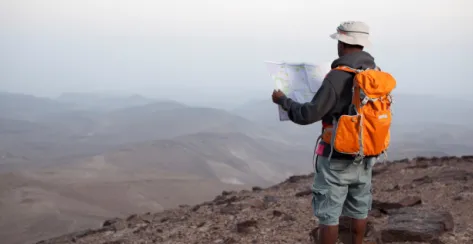Man standing and holding a map as he gazes over the top of a mountain.