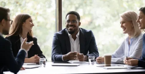 Smiling co-workers engaged in a conversation while sitting down at an office table