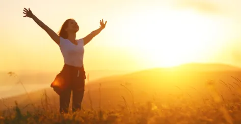 Young millennial woman stretches and is enjoying the sunrise from above a grass hill.