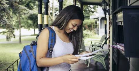 Girl with a blue backpack smiling while looking down at documents. 