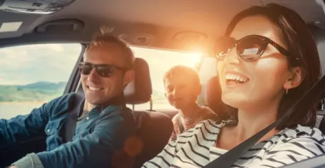 Smiling parents and their young son in the backseat riding in a car on a bright sunny day.