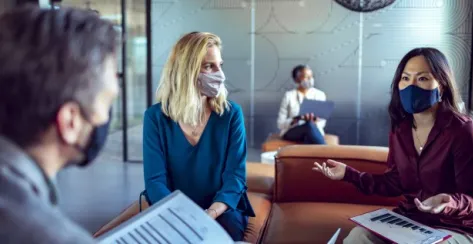 Close-up of three coworkers with facemasks and dressed in business casual meeting in a modern lobby