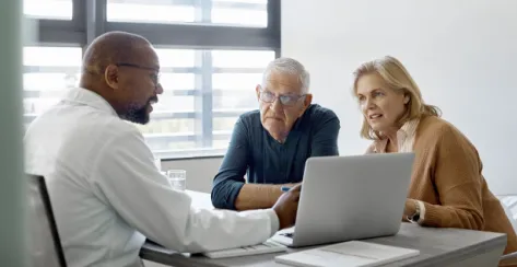 Male doctor sitting down with an older couple while pointing to his laptop screen.