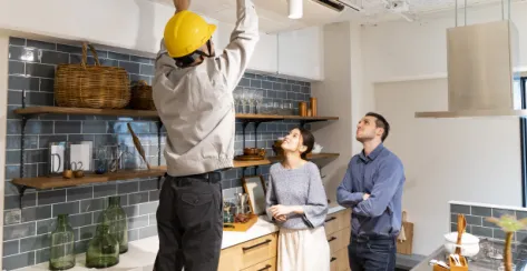 Couple watching a construction worker fix the ceiling in their kitchen