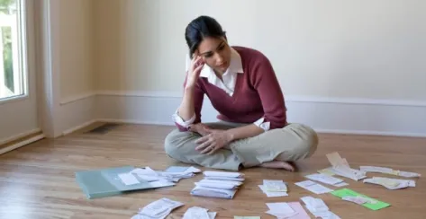 Young woman sitting on the ground looking at her financial documents that are spread out around her 