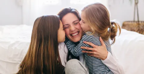 A mother with young daughters kissing either cheek.