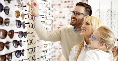 A couple with their young daughter browse glasses frame options at an optical shop.